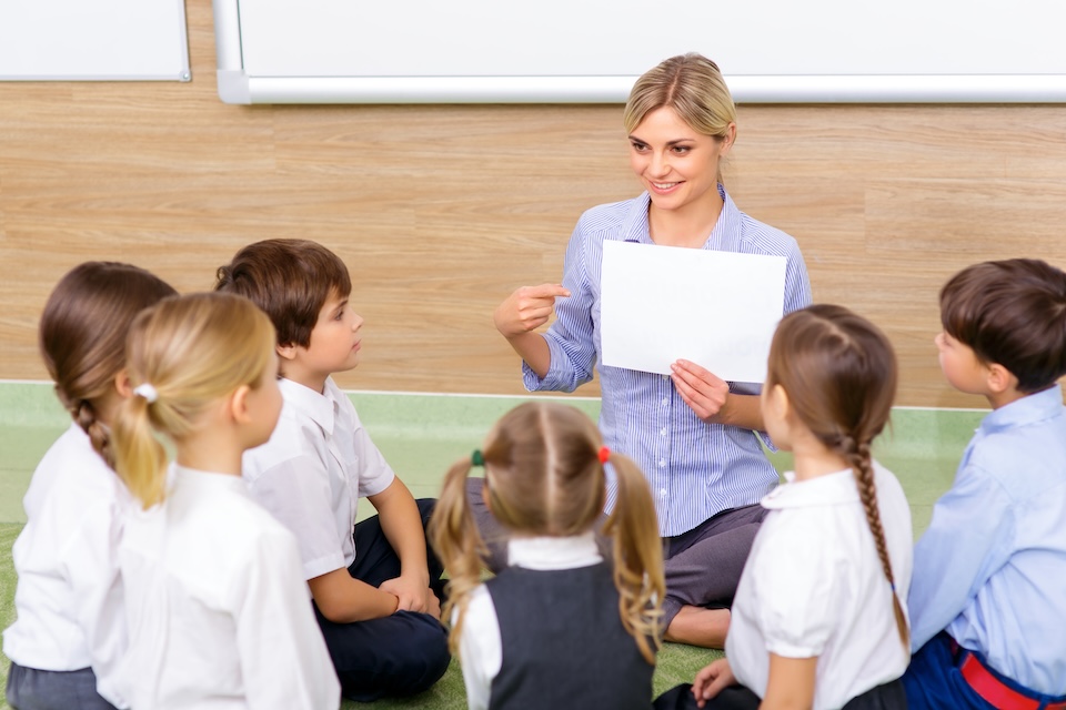 Teacher holding paper sitting with students on floor